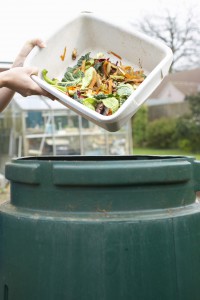 Unrecognizable person pouring kitchen waste into compost bin, close-up of hands